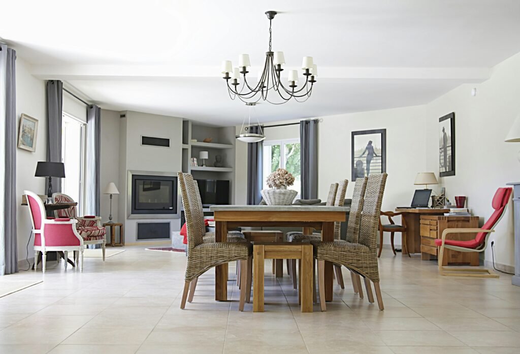 Spacious dining room with a chic chandelier, wicker chairs, wooden table, and cozy fireplace.