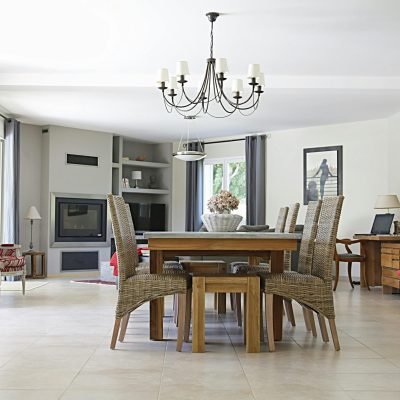 Spacious dining room with a chic chandelier, wicker chairs, wooden table, and cozy fireplace.